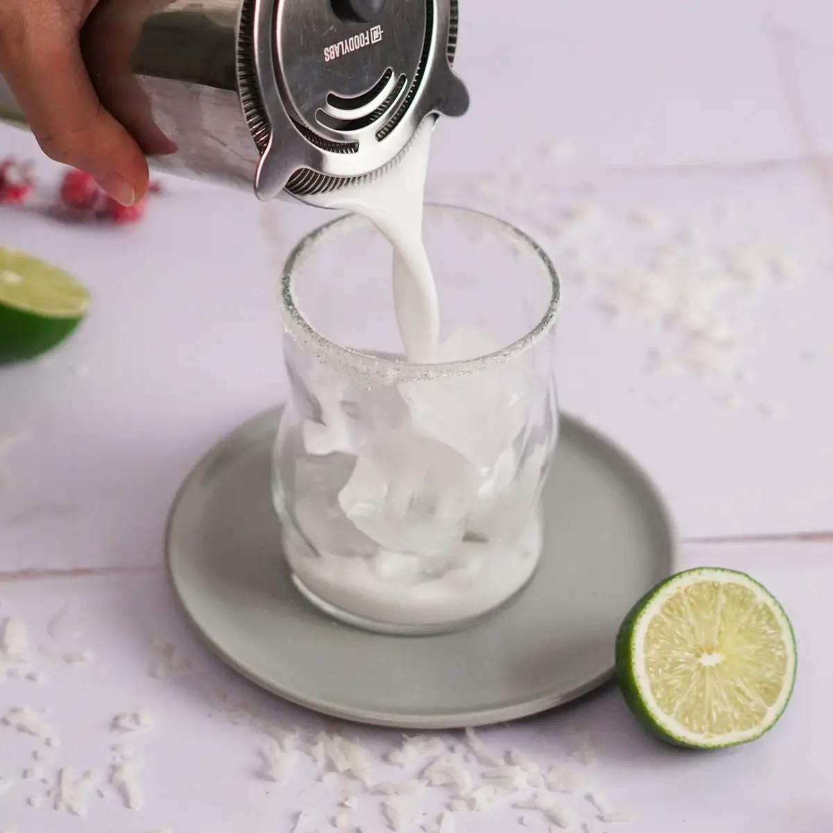 Pouring a White Christmas Margarita cocktail into a glass.