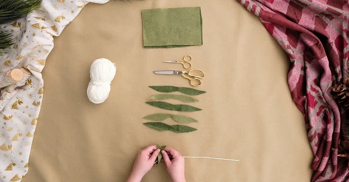 Tying leaf shapes made from felt onto a DIY Christmas garland.
