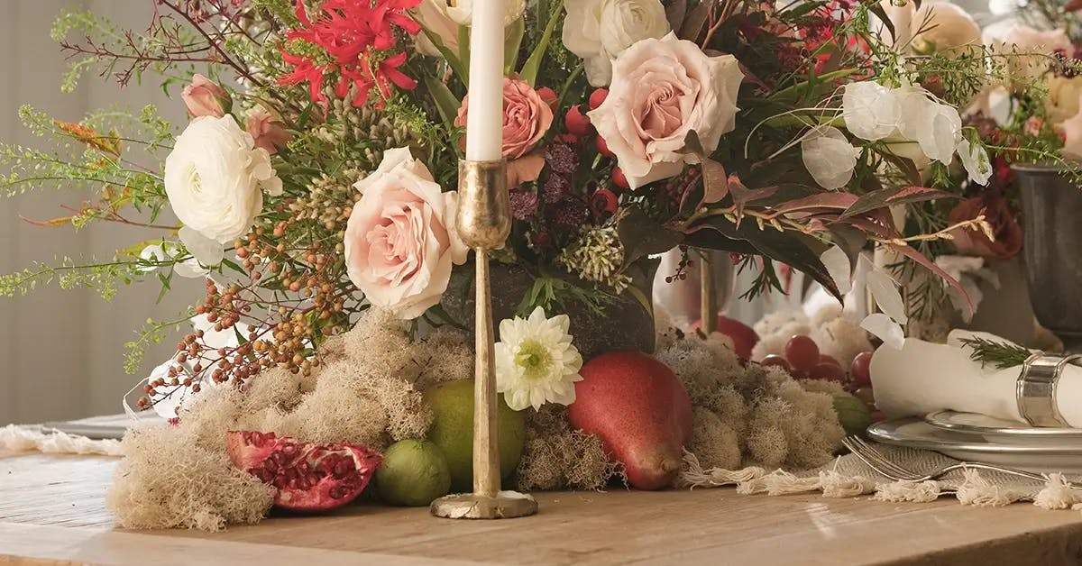 A Christmas table centerpiece with candles, surrounded by reindeer moss and fruit.