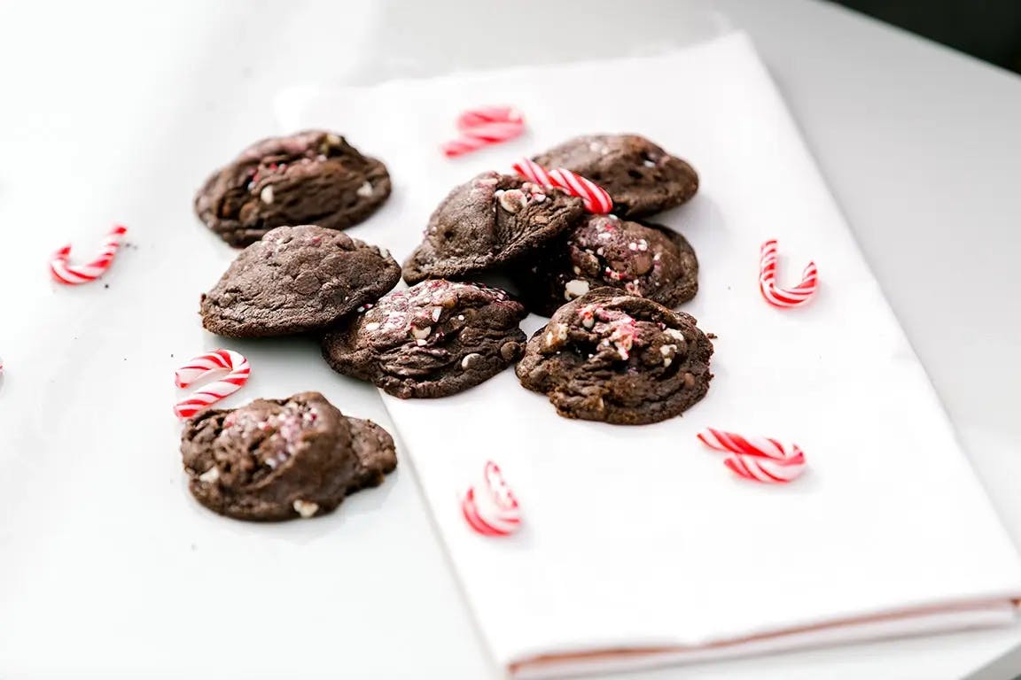 Chocolate peppermint cookies on a napkin, with candy canes scattered around.