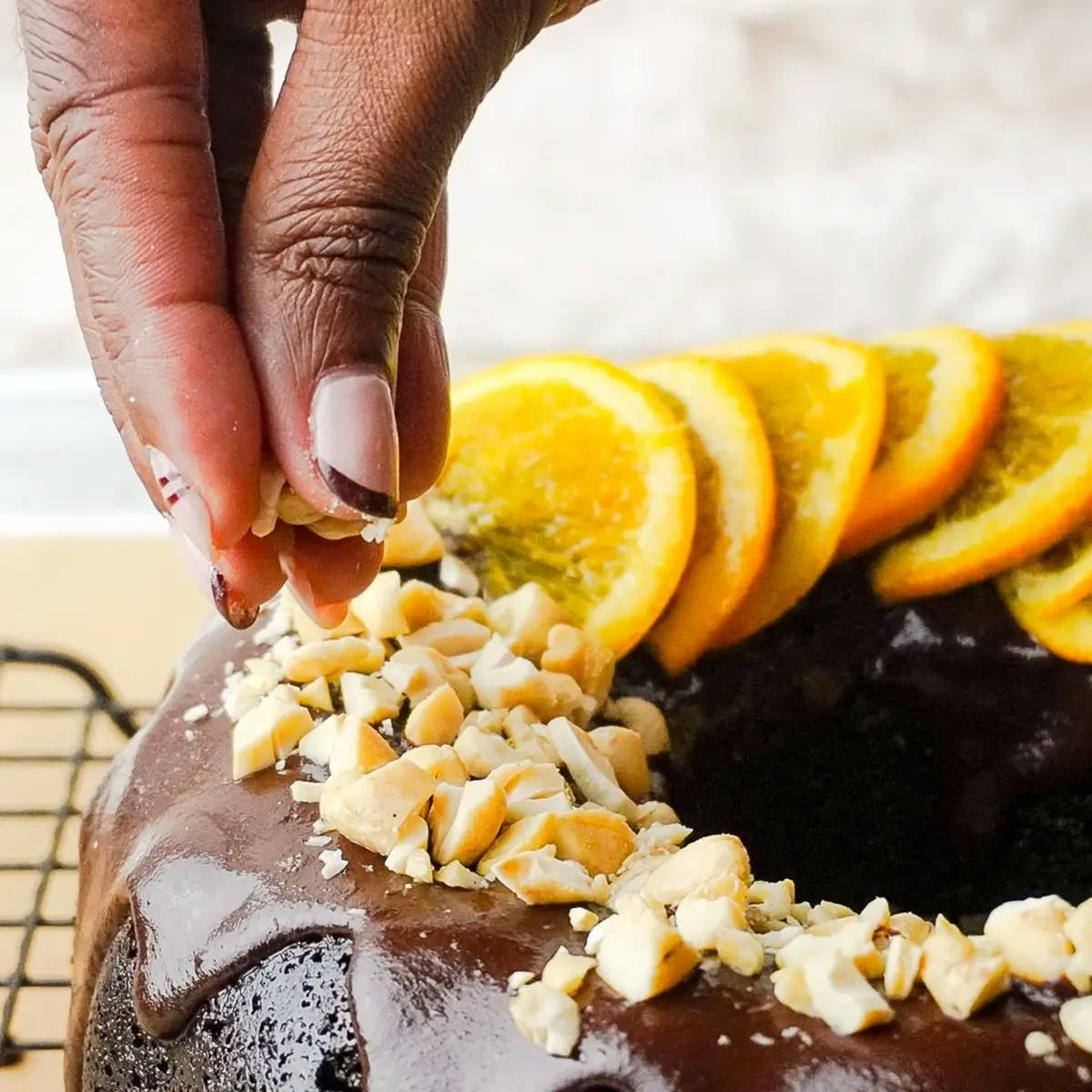Fingers garnishing a vegan chocolate orange bundt cake with orange slices and nuts.