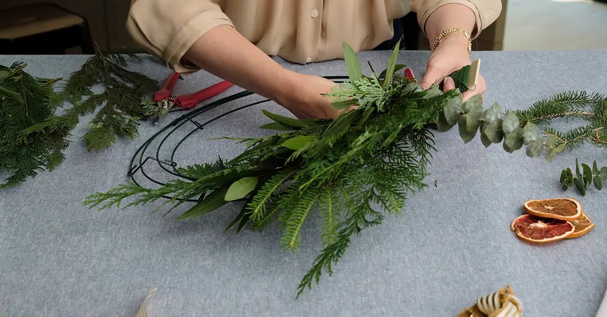 Adding a bundle of greens to the wire form of a Fall wreath.