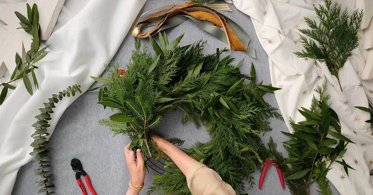 Securing greens to a winter wreath with wire.