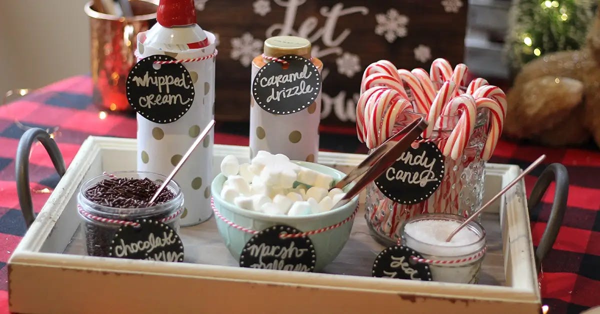 Hot chocolate topping station, showing whipped cream, caramel drizzle, candy canes, chocolate sprinkles, marshmallows, and sea salt.