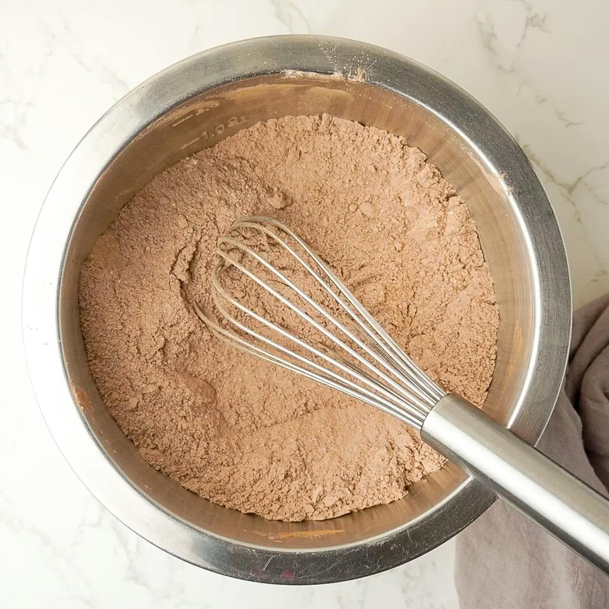 Cocoa, sugar, flour, and other dry ingredients in a bowl. Part of a recipe for Vegan Chocolate Orange Cake.