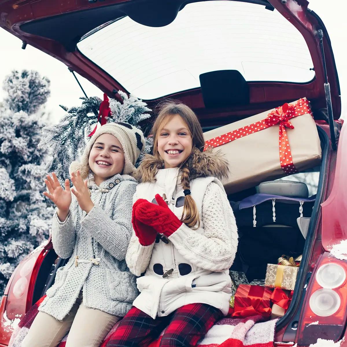 Two girls sitting in the back of a car filled with Christmas gifts