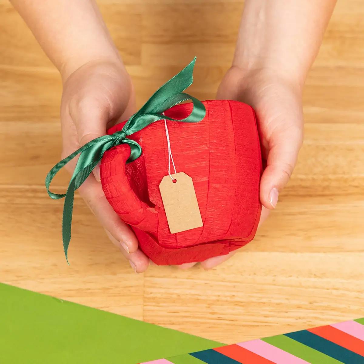 A mug wrapped in red cree paper with green ribbon tied around the handle.