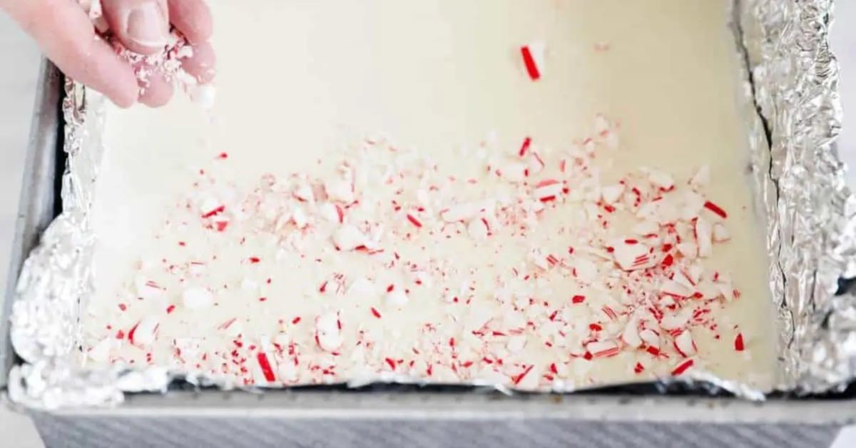 Crushed candy canes being added to the white chocolate layer of Christmas peppermint bark.