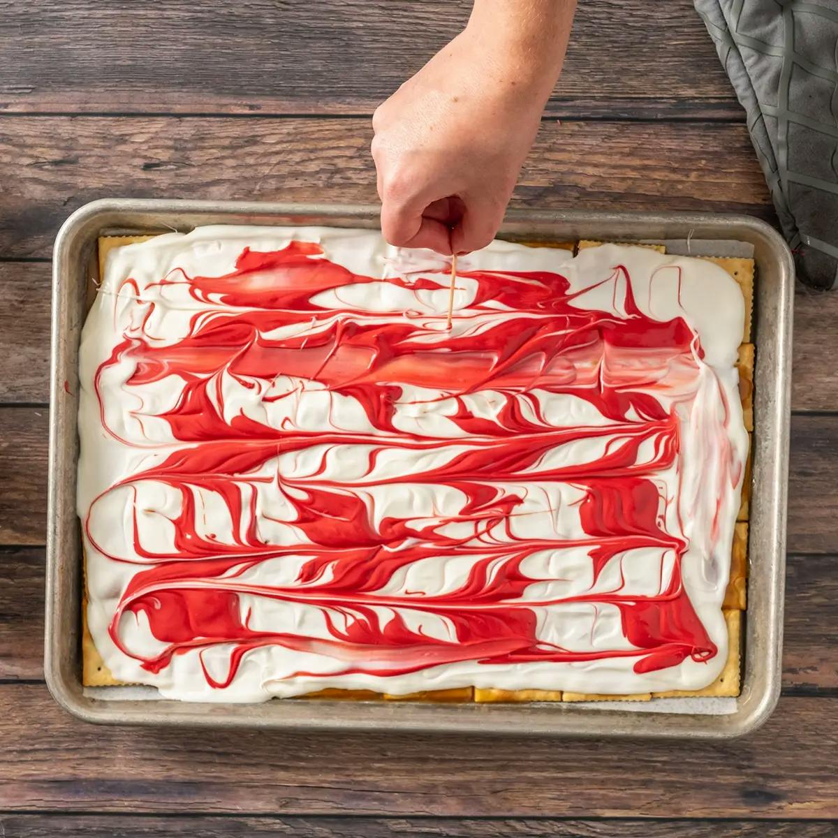Swirling white chocolate and red candy together on the top of Christmas Crack.