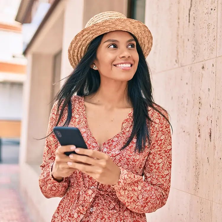 Hispanic woman in red dress and sun hat, holding phone
