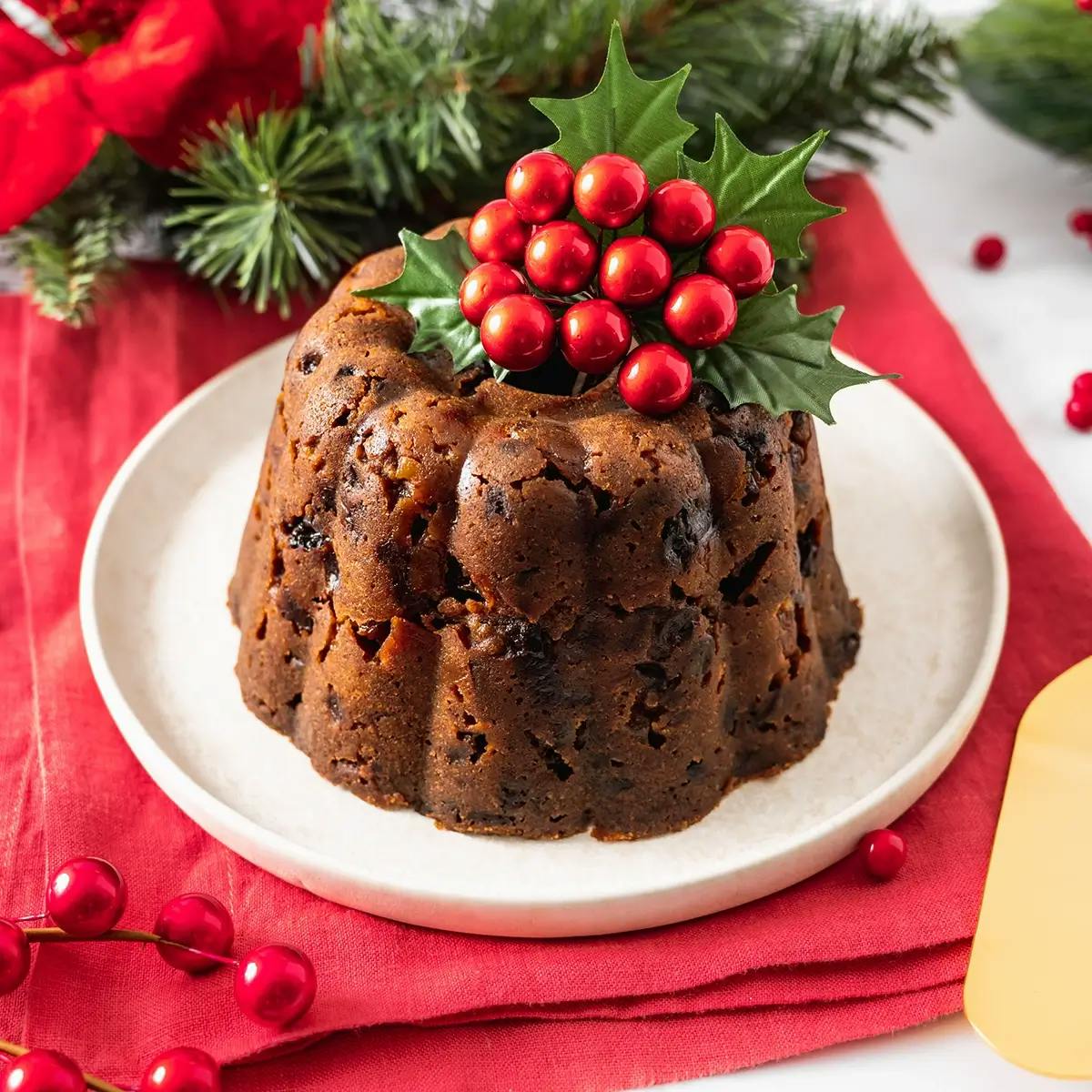 A traditional Christmas Plum Pudding on a plate, with a sprig of holly on the top.