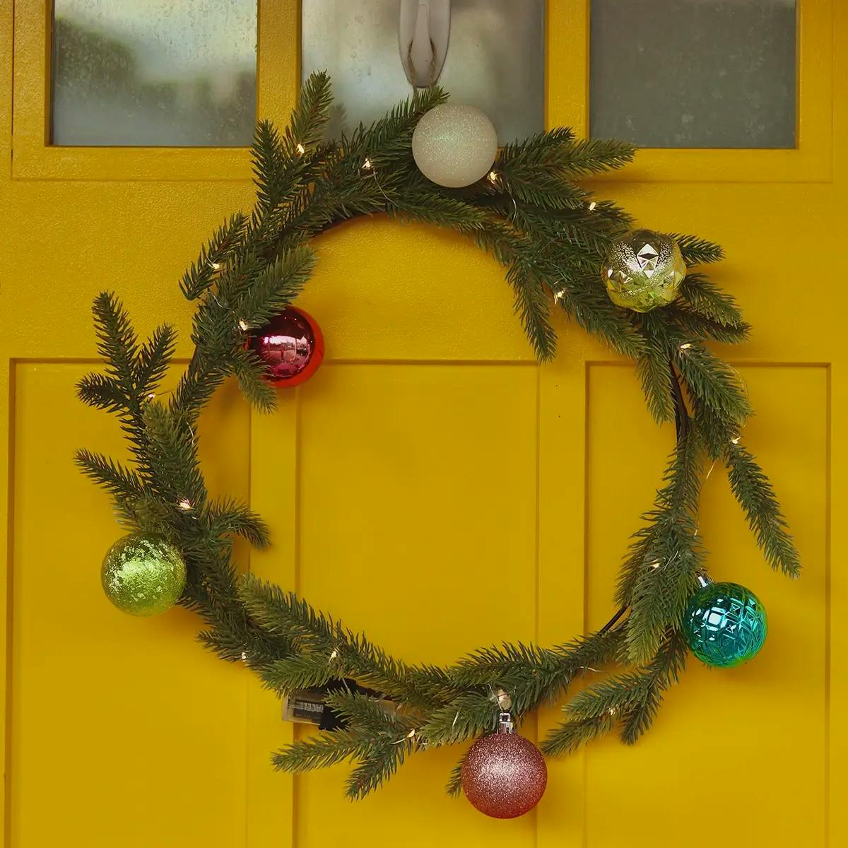 A contemporary yellow door with a simple wreath with primary-colored bulbs.