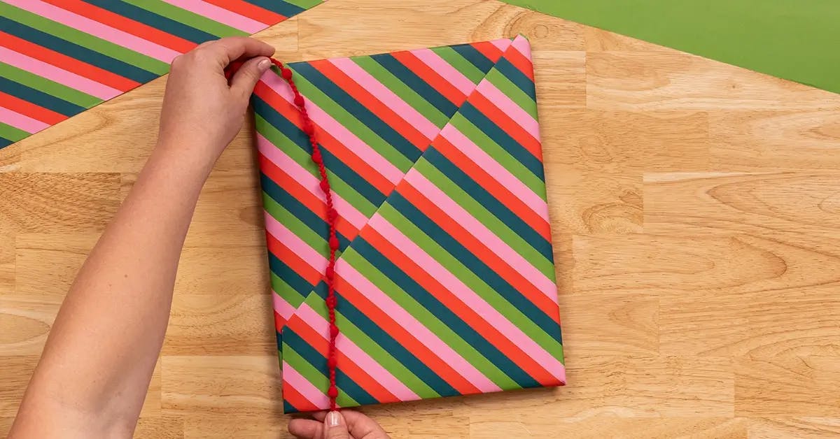 Adding a final ribbon to a book wrapped in Christmas wrapping paper.