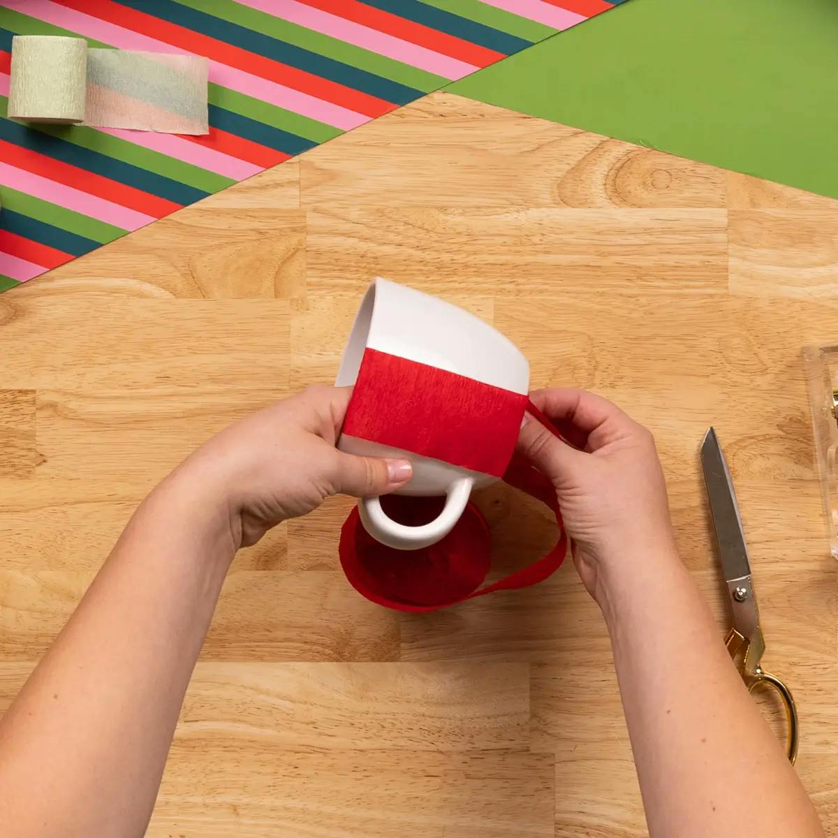 Measuring the height of a coffee cup with crepe paper, as part of a tutorial on how to wrap a mug.