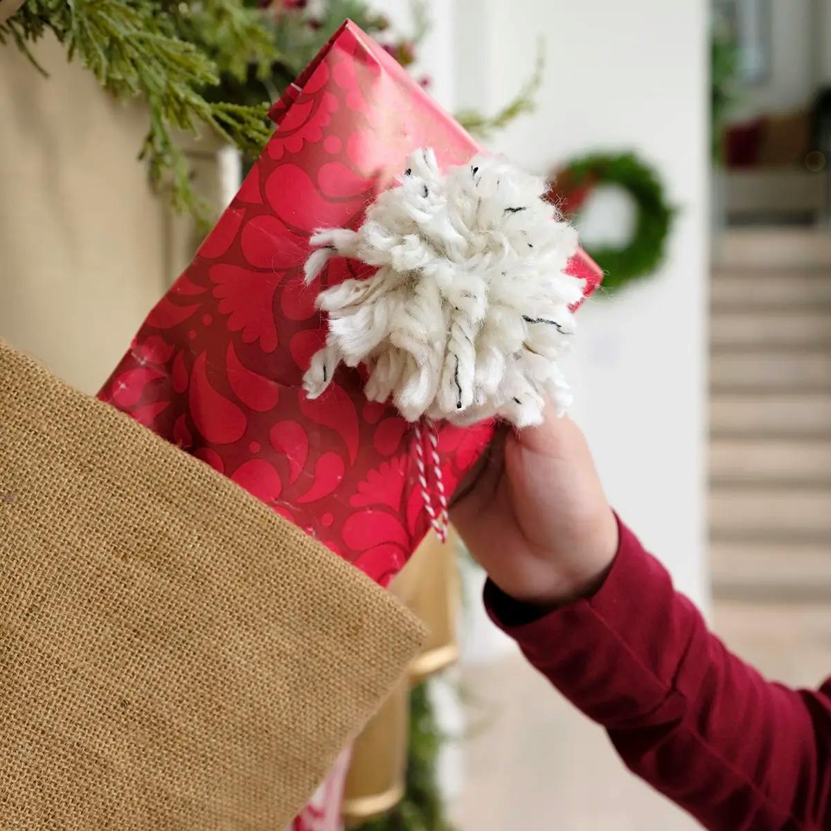 A hand placing a gift into a stocking, in a gift bag made from wrapping paper.