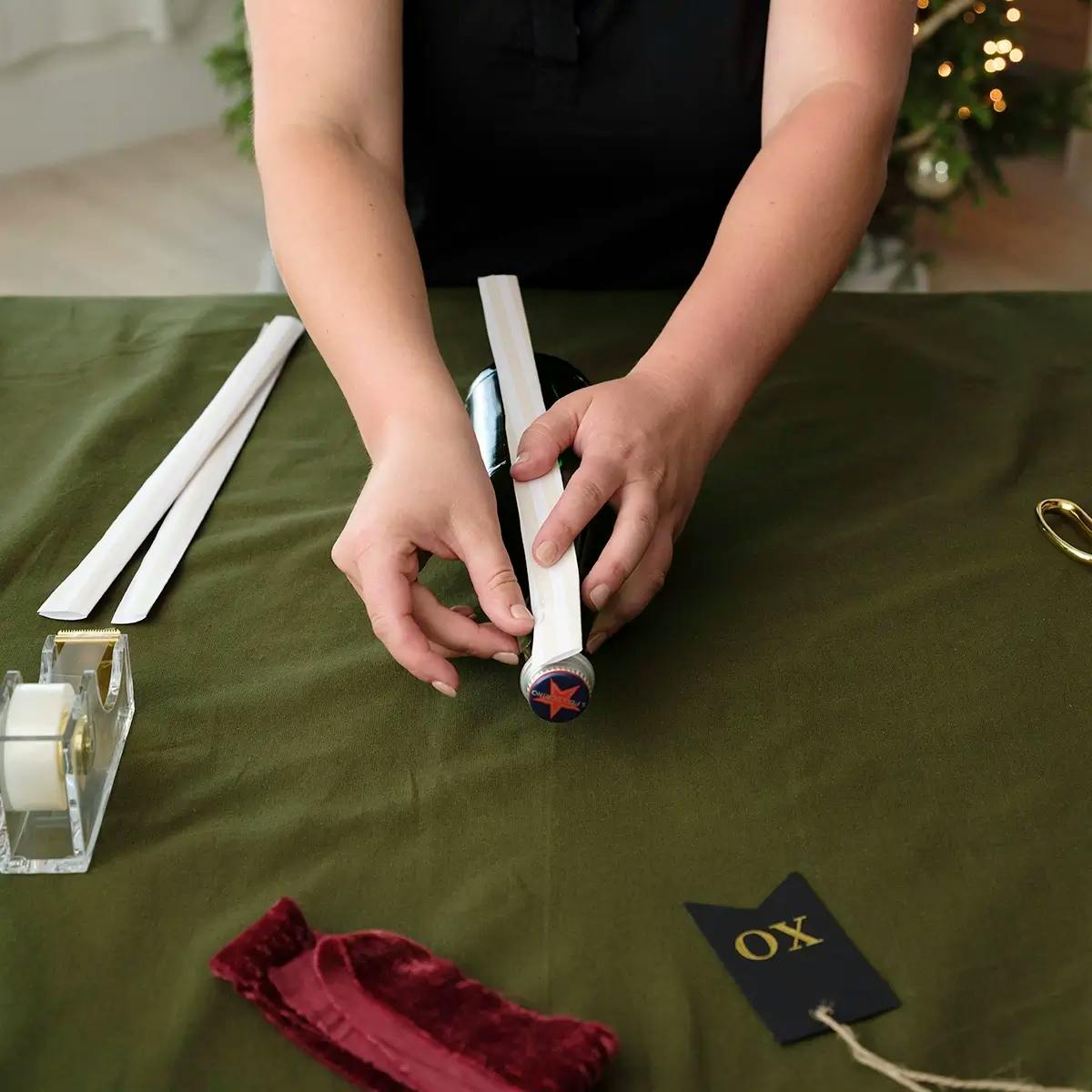 Taping wrapping paper to a wine bottle.