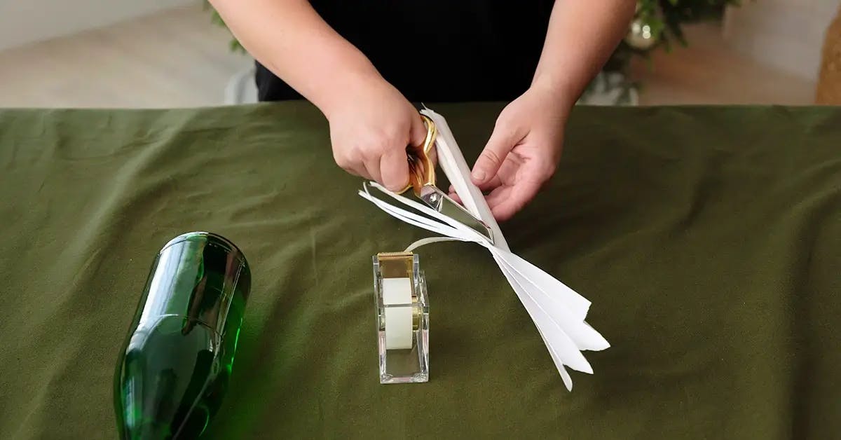 Cutting folded wrapping paper into strips ready to wrap a wine bottle.