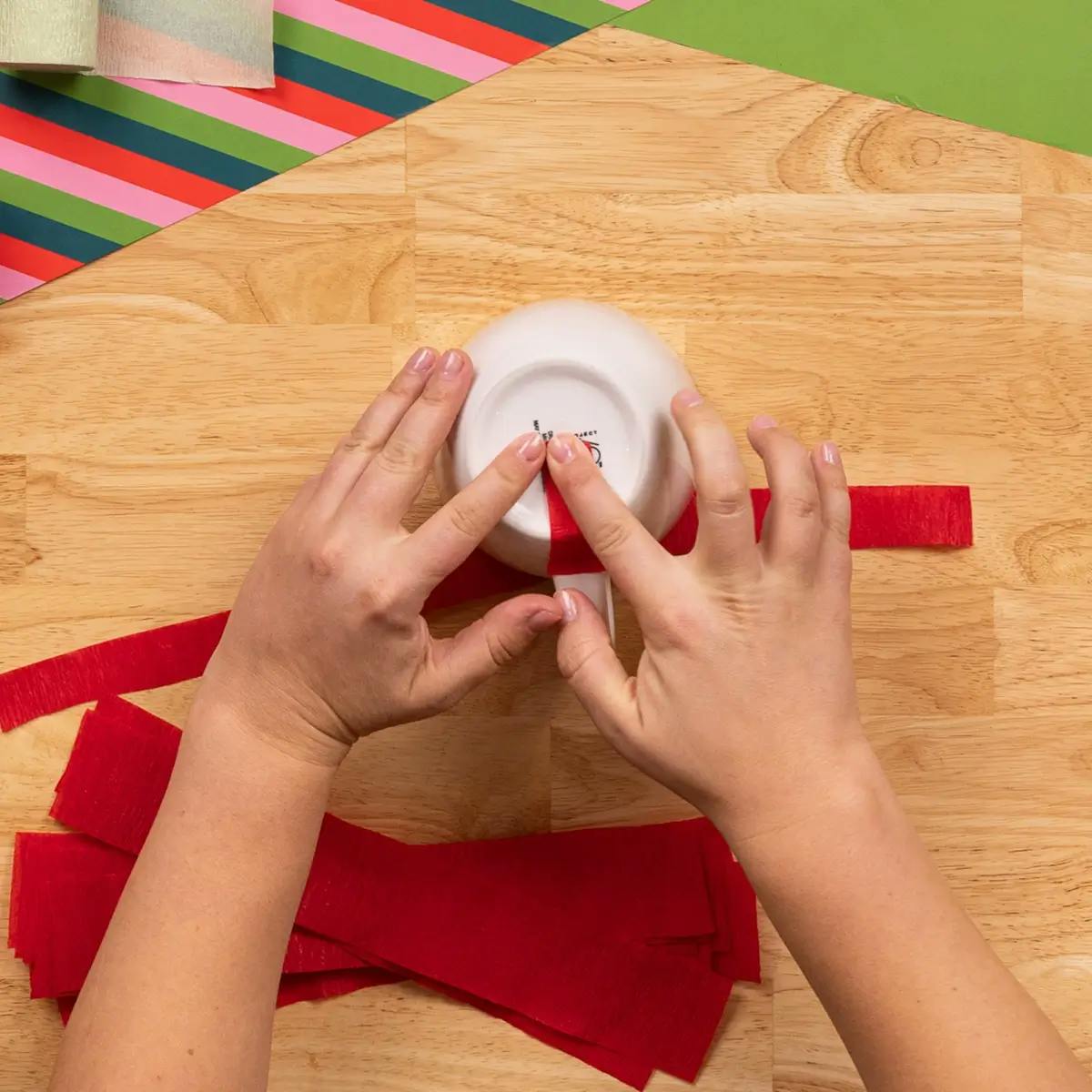 Attaching crepe paper to the bottom of a mug, in a tutorial on how to wrap a mug.