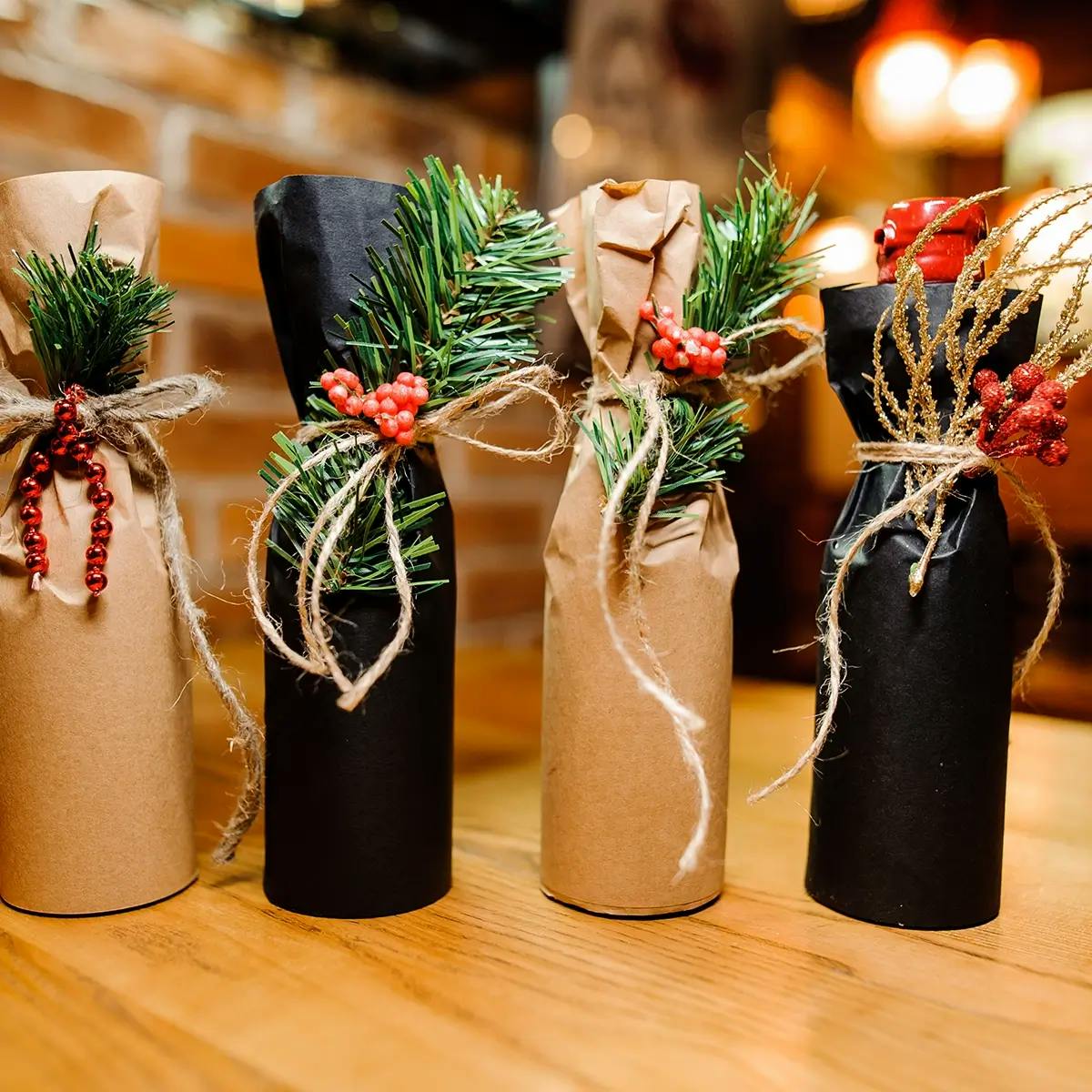 Four bottles of wine, wrapped in brown paper tied with ribbon and decorated with spruce and berries.