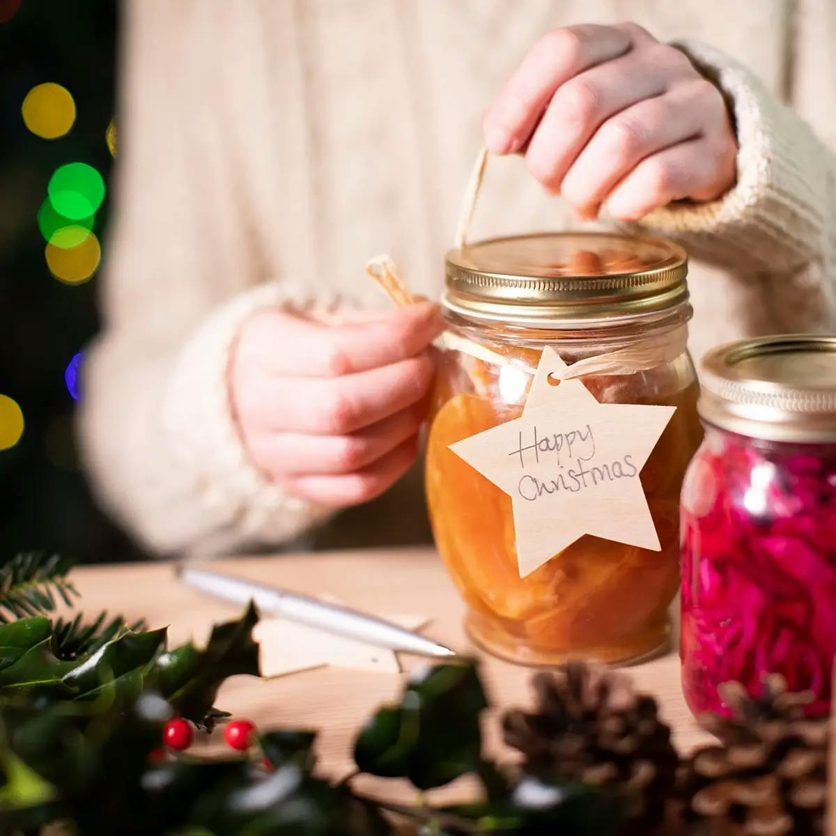 Hands tying a reusable wooden gift tag on homemade jars of preserves for a handmade Christmas gift on a budget.