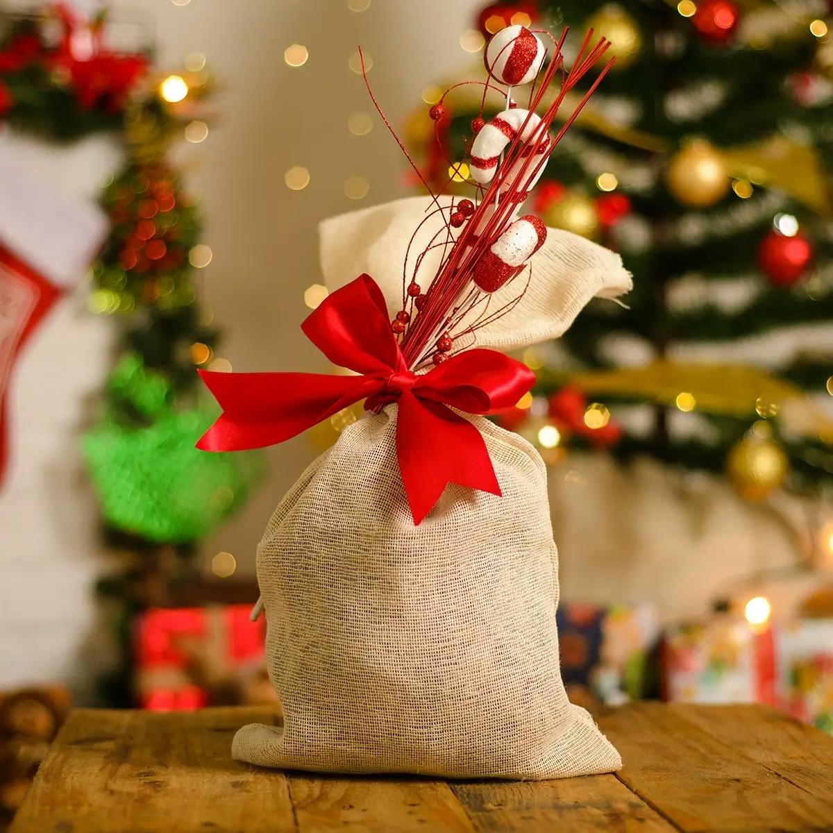Hessian Christmas goodie bag tied with red ribbon, with Christmas tree in the background.