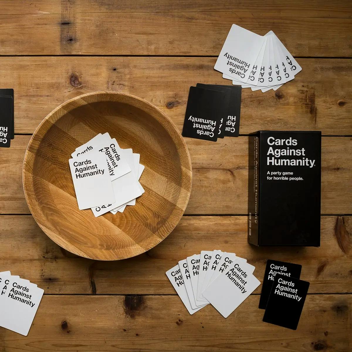 Cards Against Humanity cards spread out on a wooden table with a wooden platter in the middle.