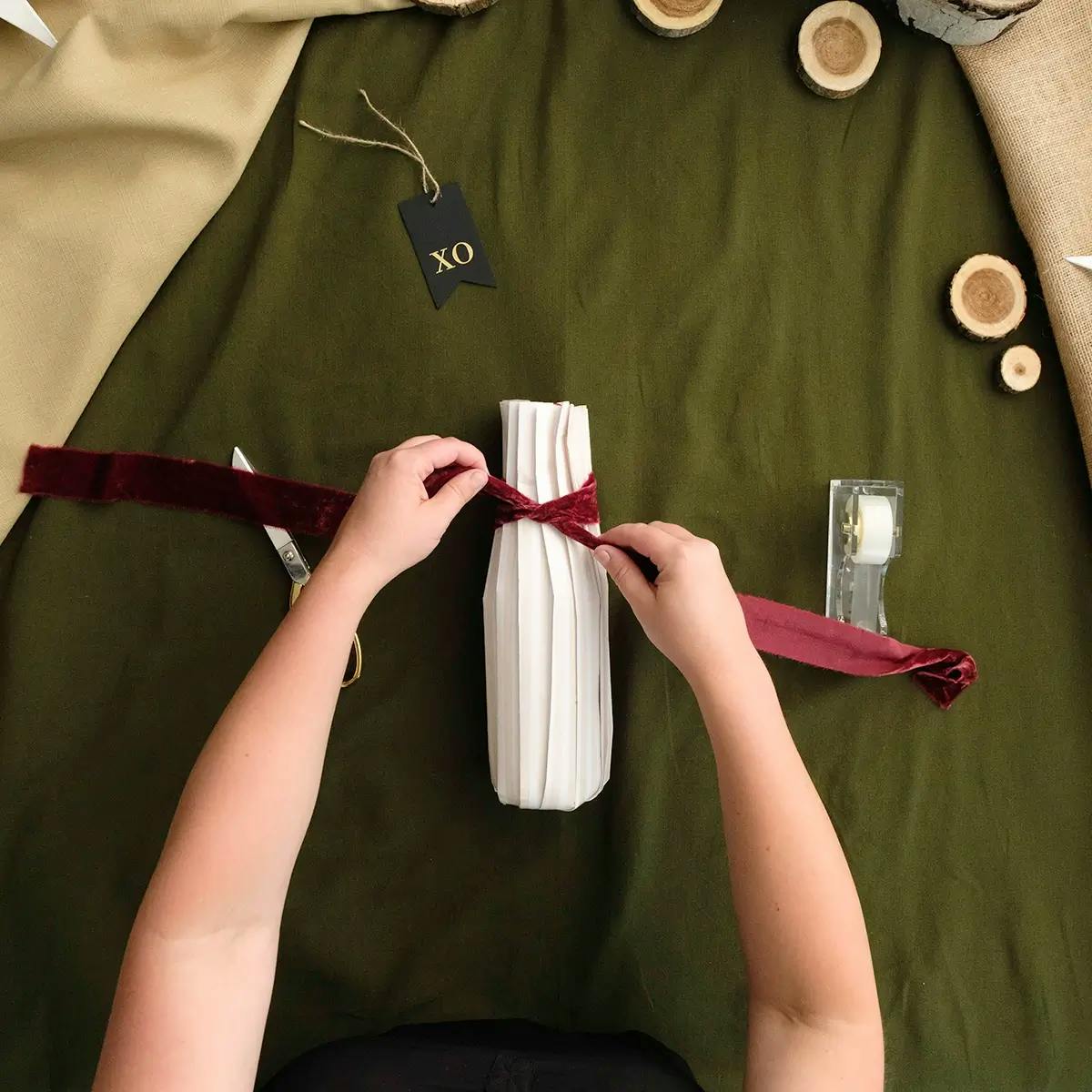 Tying a velvet ribbon around the neck of a wine bottle wrapped in pleats.