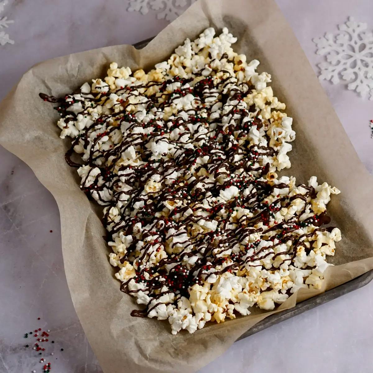 Christmas popcorn on a baking tray, drizzled with peppermint dark chocolate and sprinkles.