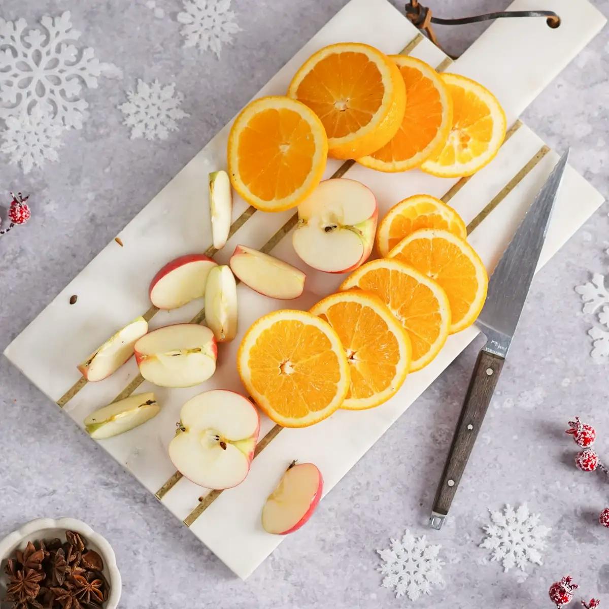 Sliced apples and oranges on a cutting board, part of a holiday punch recipe.
