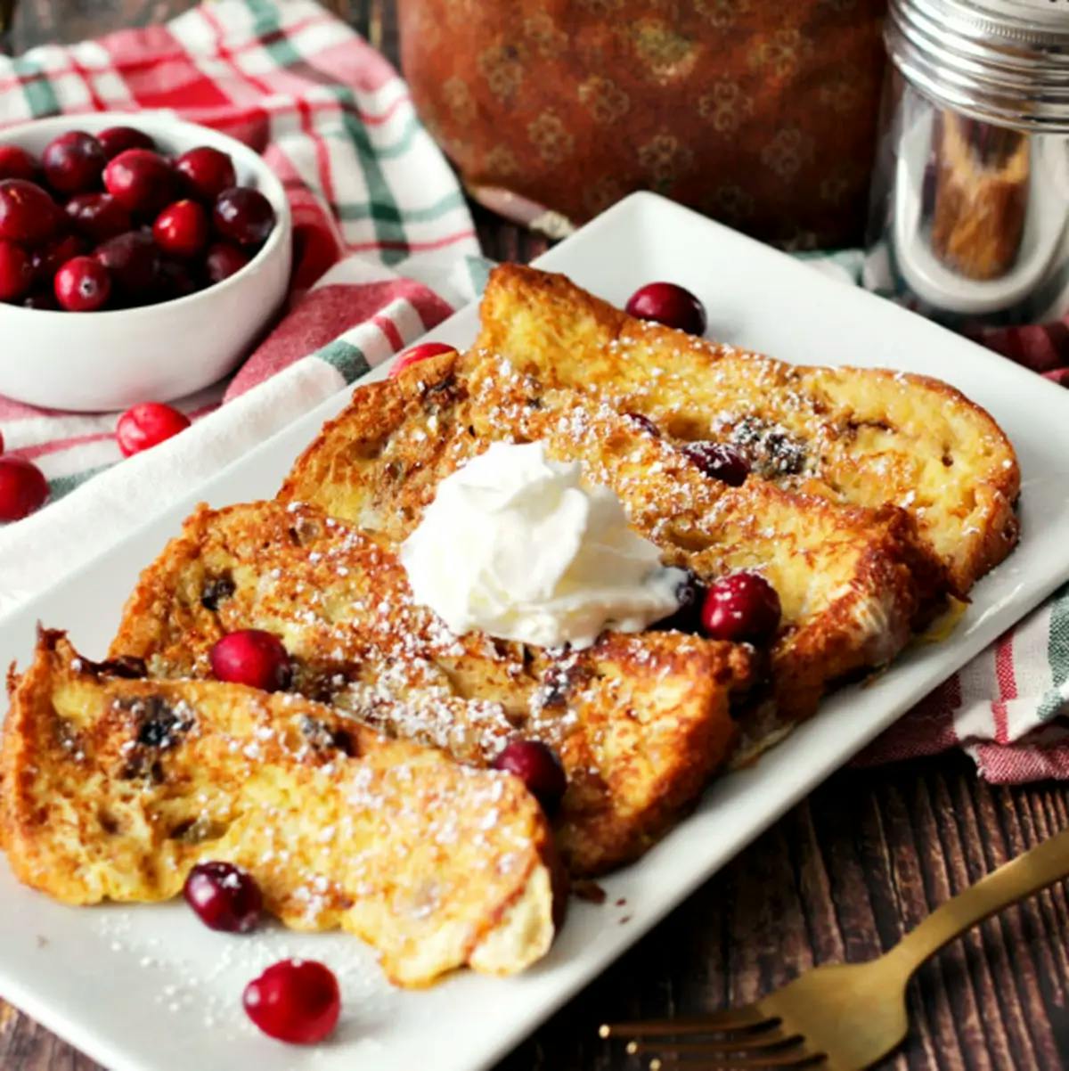 French toast made from panettone on a plate topped with cranberries and whipped cream.