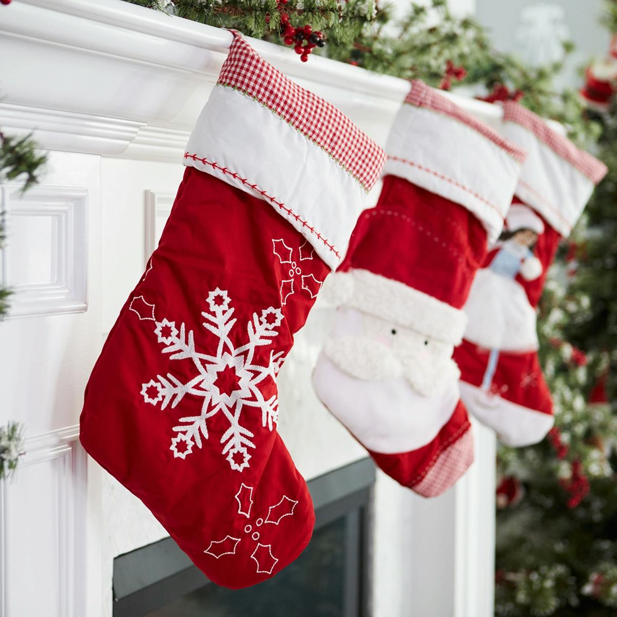 Red and white festive Christmas stockings hanging diagonally on a mantel. From foreground to background: Stocking with snowflake, stocking with Santa and stocking with festive holiday girl.
