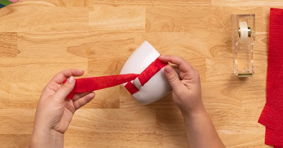 Wrapping a piece of crepe paper around the handle of a coffee cup, in a tutorial on how to wrap a mug.
