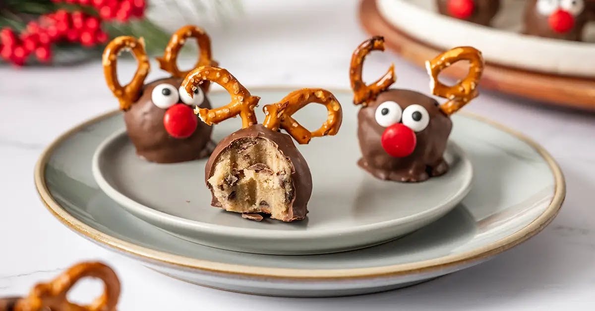 Reindeer Cookie Dough Balls covered in chocolate with pretzel pieces for antlers and mini M&Ms as eyes and nose.