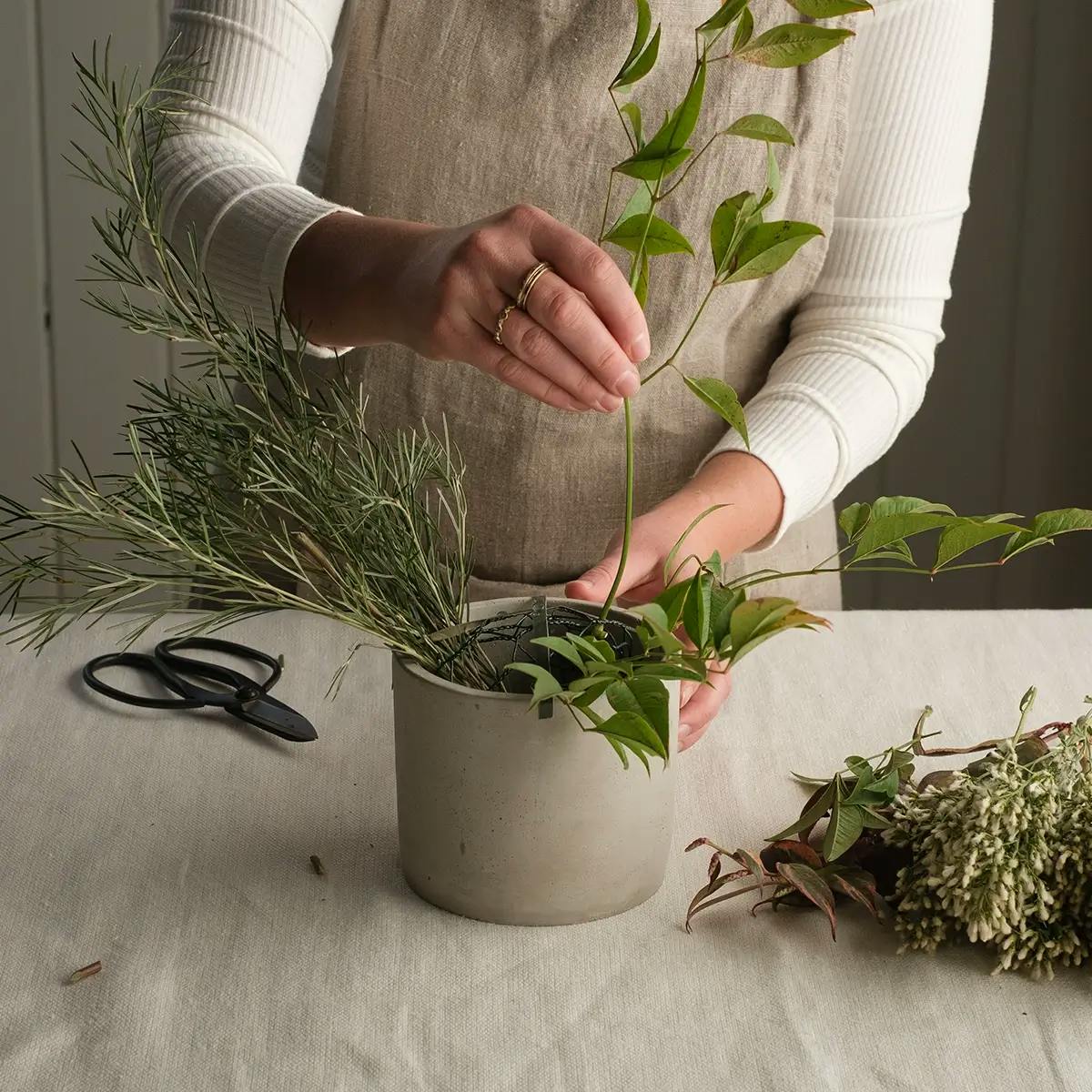 Hands adding greenery to a vase for a Christmas centerpiece.