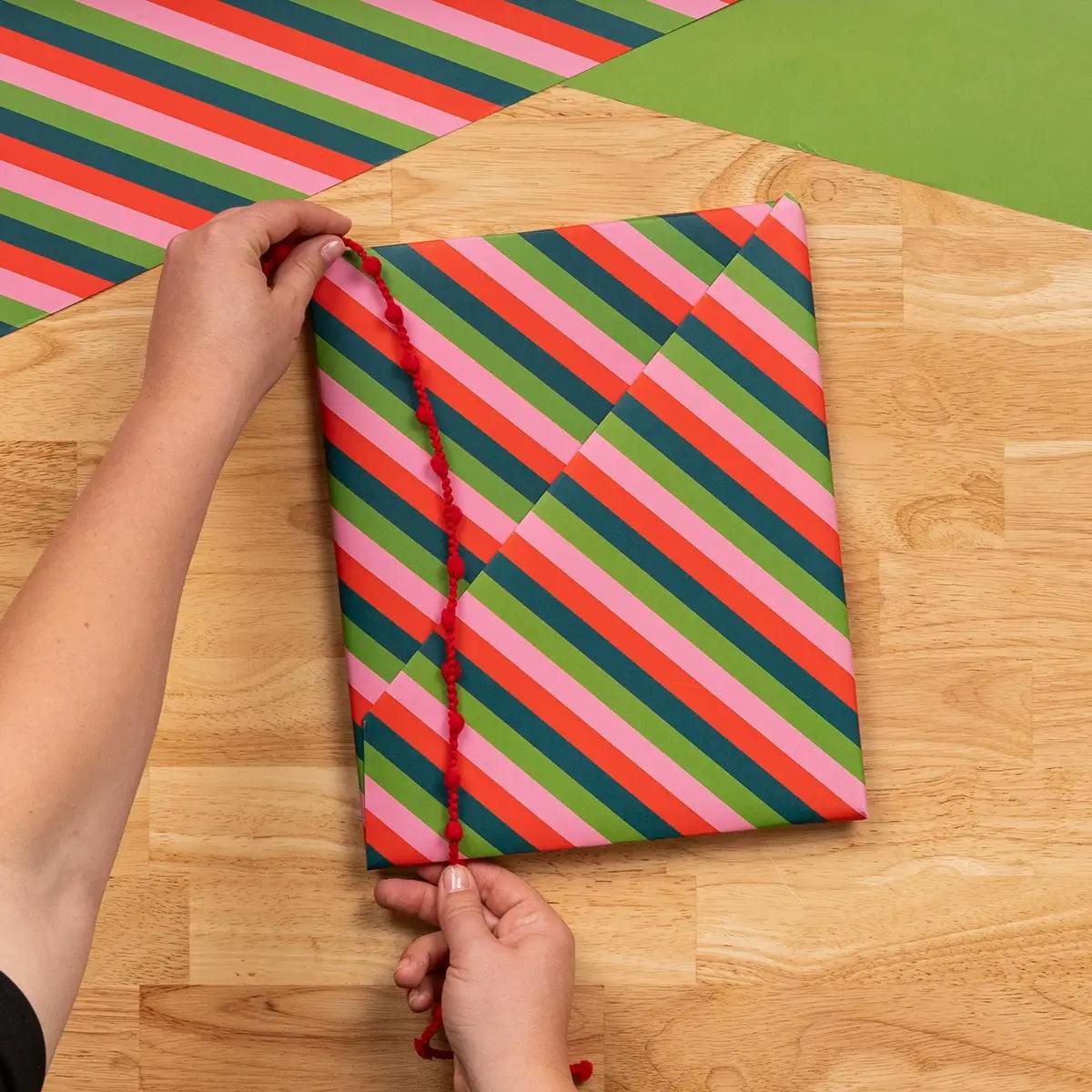 Adding a final ribbon to a book wrapped in Christmas wrapping paper.