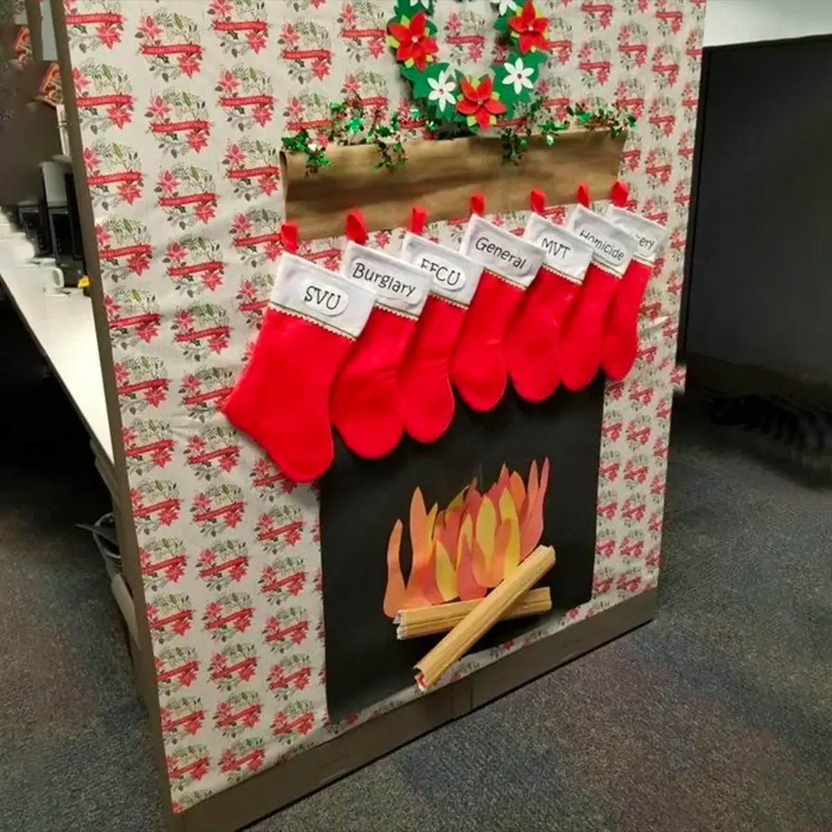 Cubicle wall decorated to look like a fireplace, with stockings hung on the mantelpiece.