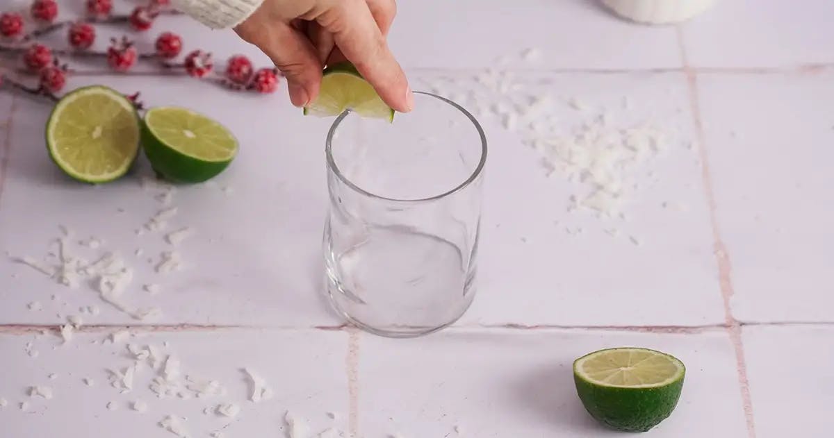 A hand using a lime to wet the rim of a glass ready for a Christmas margarita.