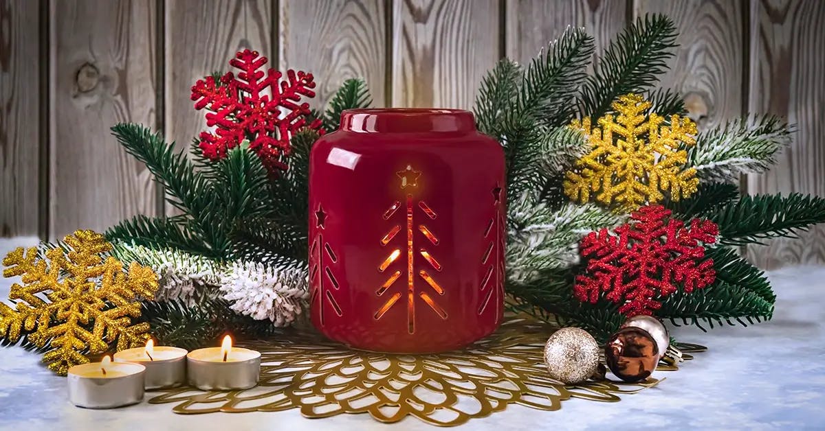 A red oil warmer on porch surrounded by Festive Christmas greens and decor.