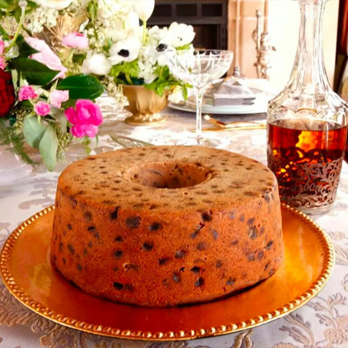 A bourbon-soaked fruit cake on a platter with a decanter of bourbon in the background.