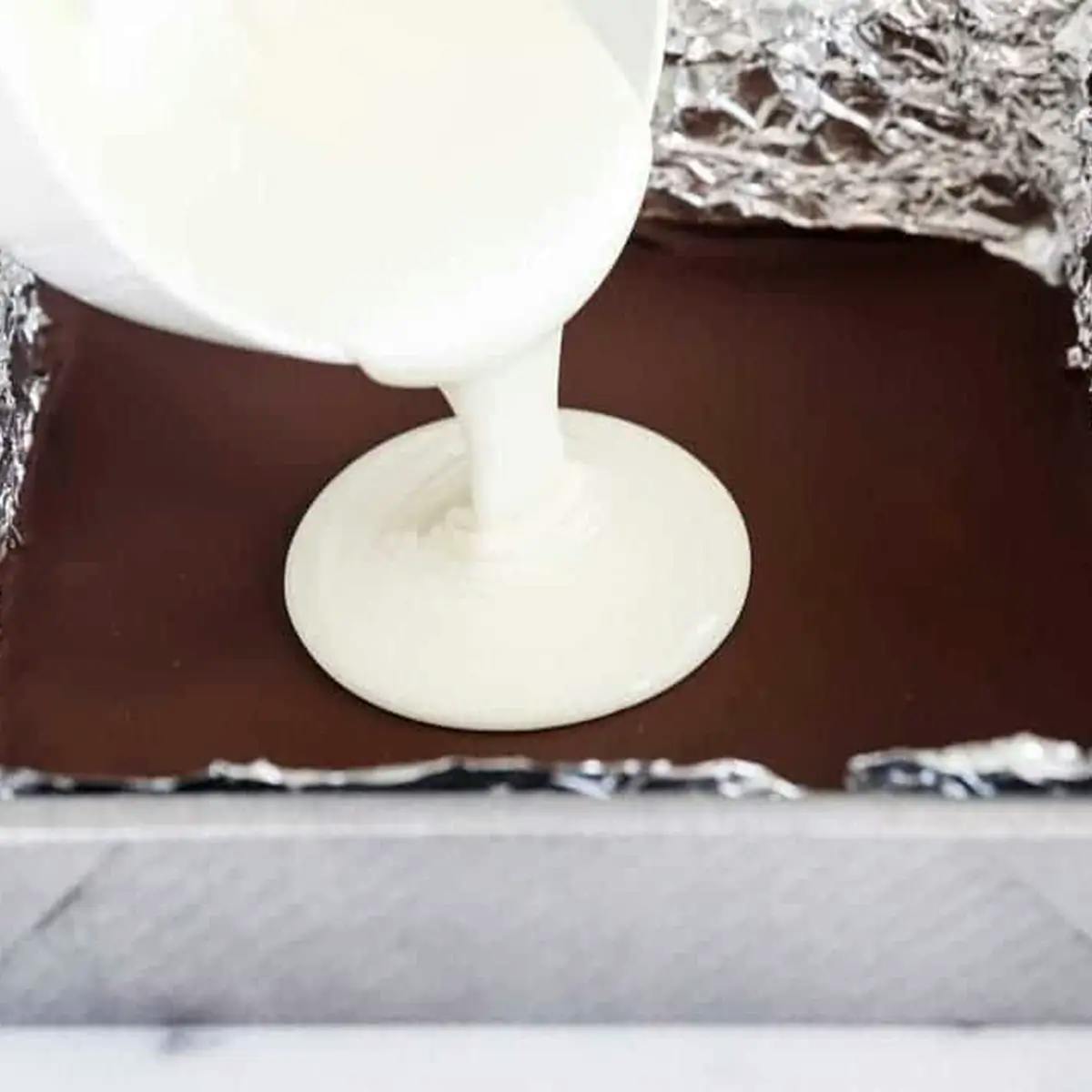 White chocolate being poured over hardened dark chocolate to make peppermint bark.