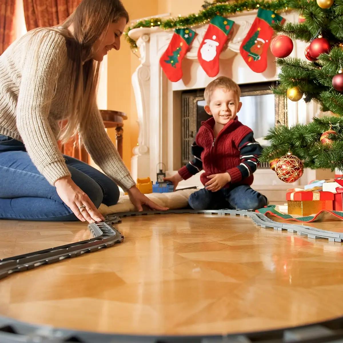 Mother and son play with model train set under Christmas tree.