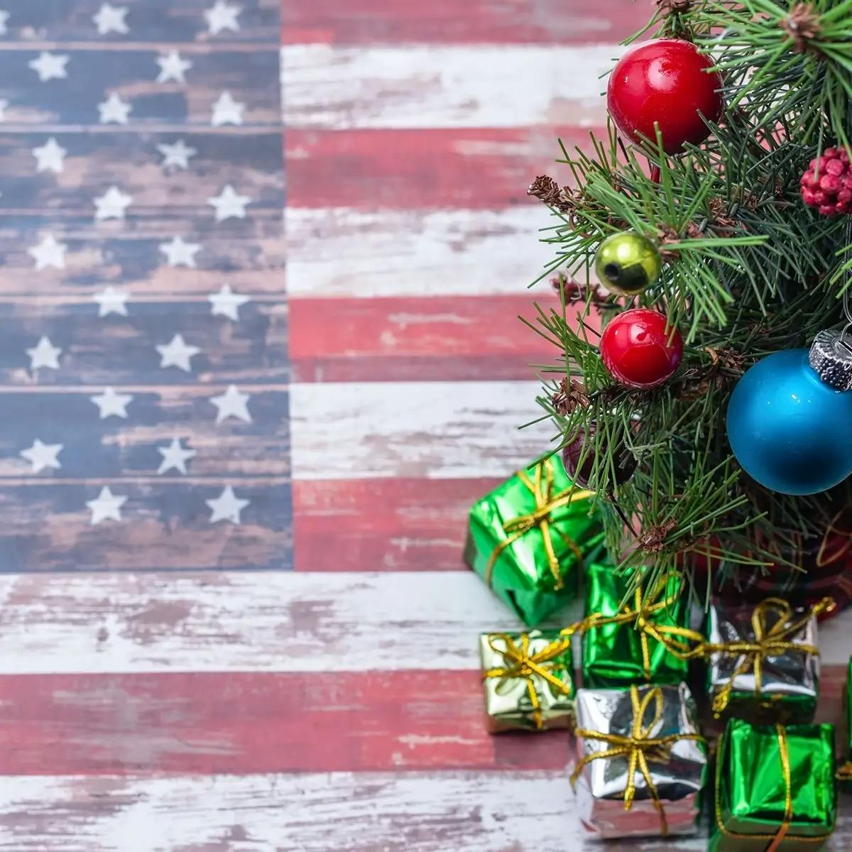 A US flag painted on wood, with a small Christmas tree and presents on top.