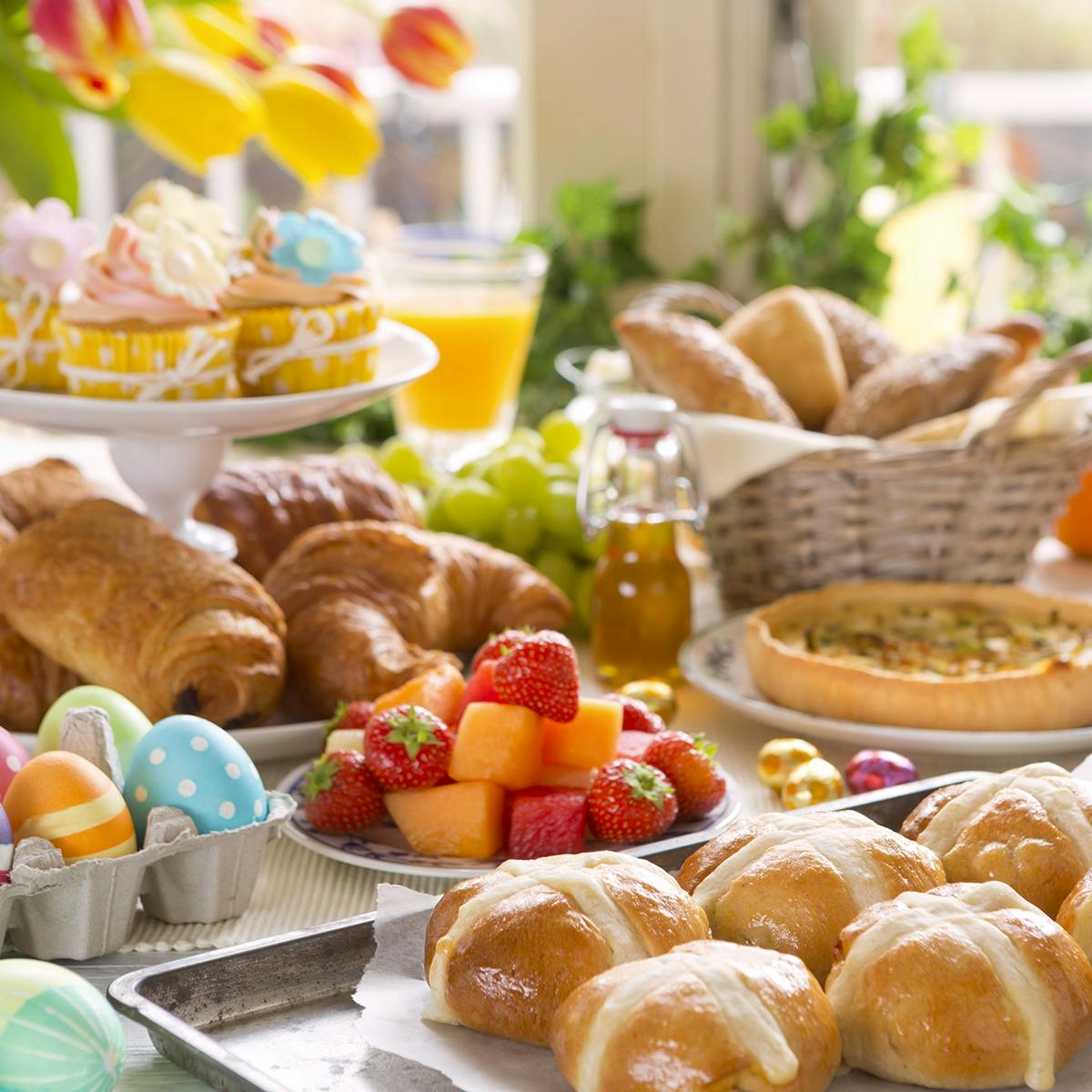Spring table set for Easter brunch with fruit, croissants, and hot cross buns