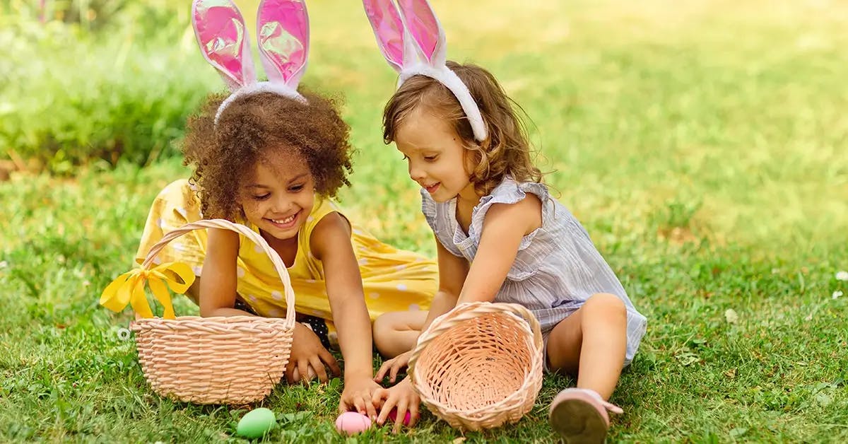 Two young girls with Easter baskets, finding eggs during an Easter egg hunt.