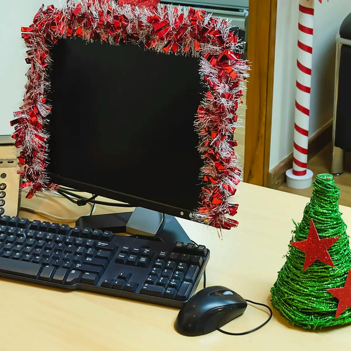 Computer screen draped in garland with a small Christmas tree on the desk to the right. 