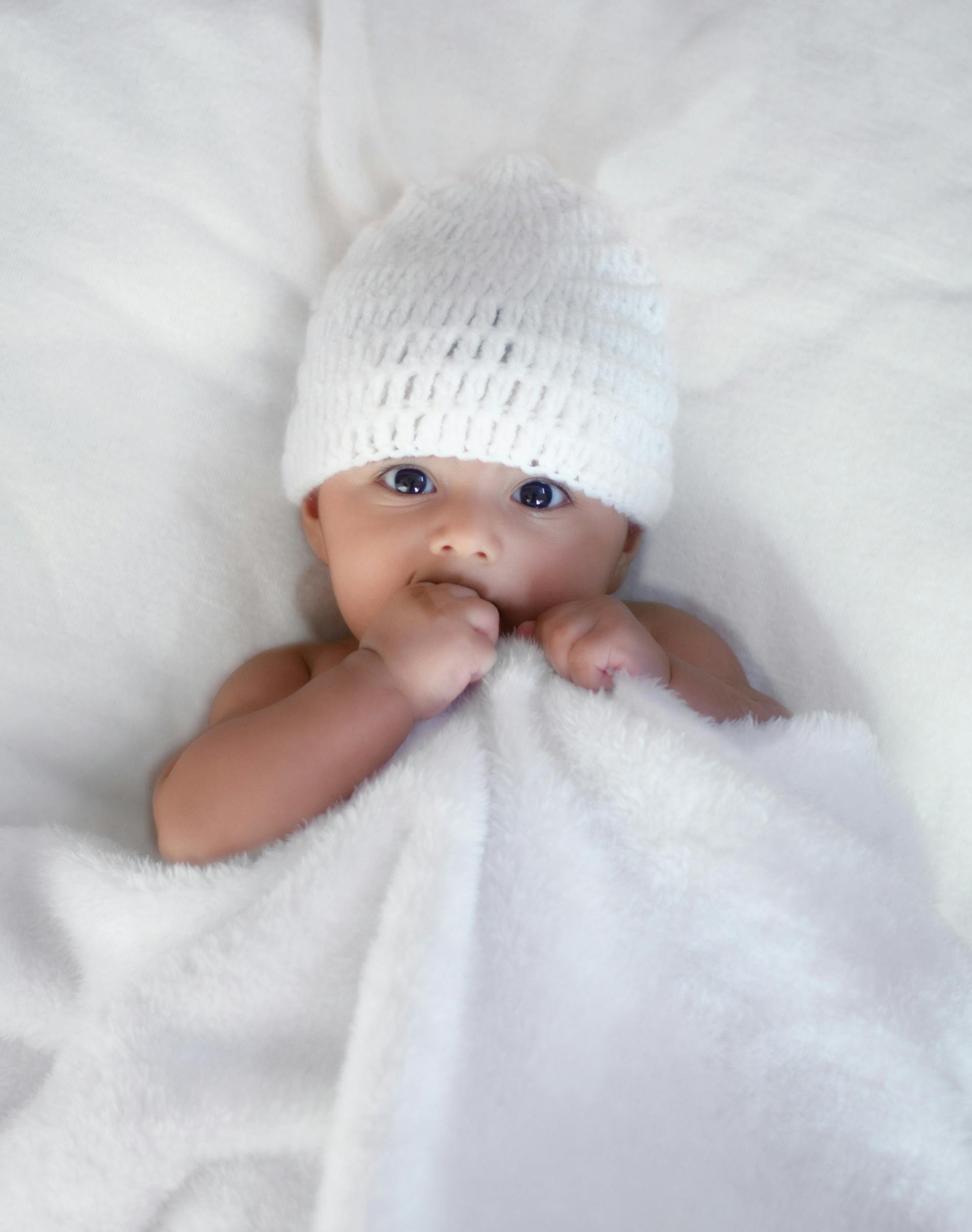 baby wrapped in a white blanked wearing a white hat