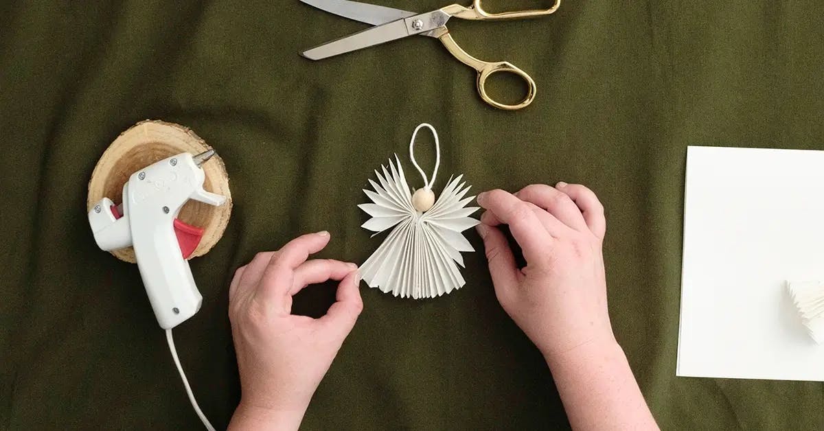 Gluing the angel wings to the body in a DIY Christmas ornament.