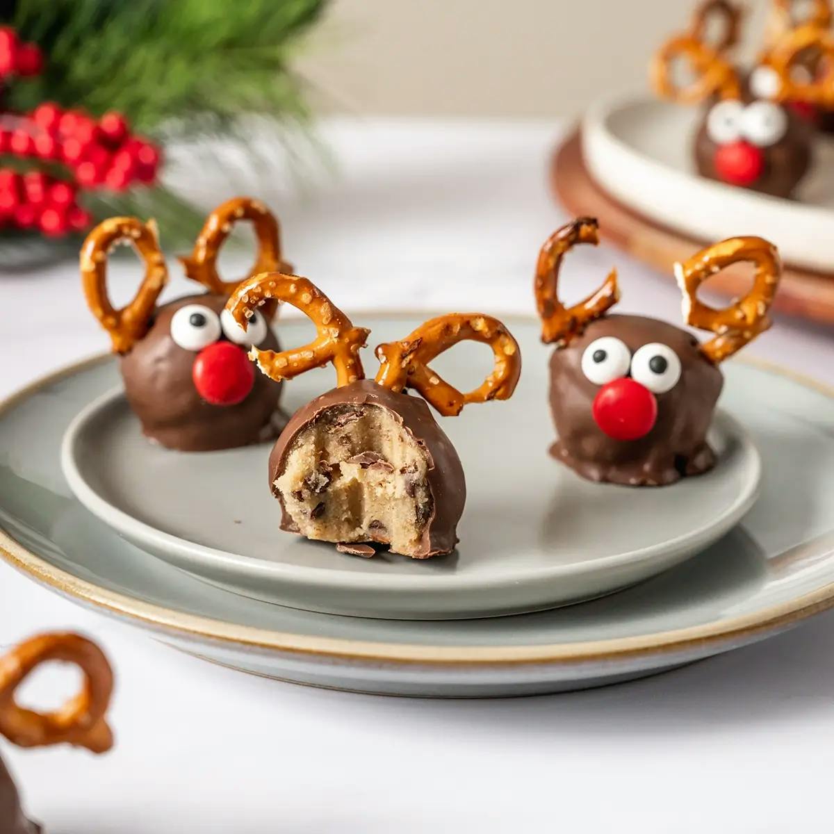 Reindeer Cookie Dough Balls covered in chocolate with pretzel pieces for antlers and mini M&Ms as eyes and nose.