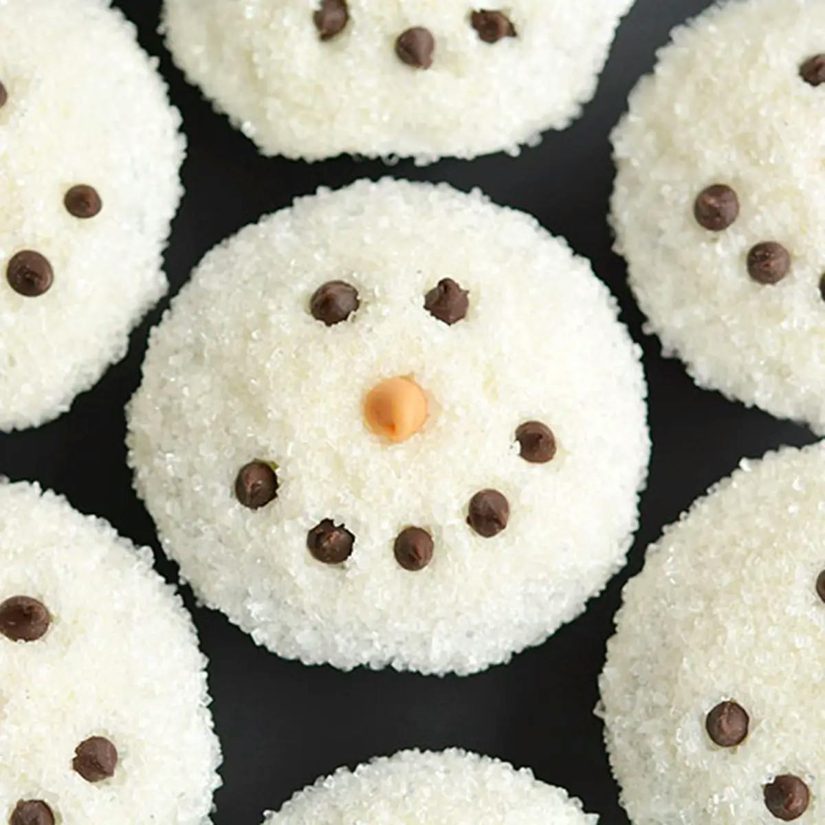 Sparkly snowman cupcake with white sugared frosting, brown dotted eyes and smile and an orange carrot nose.