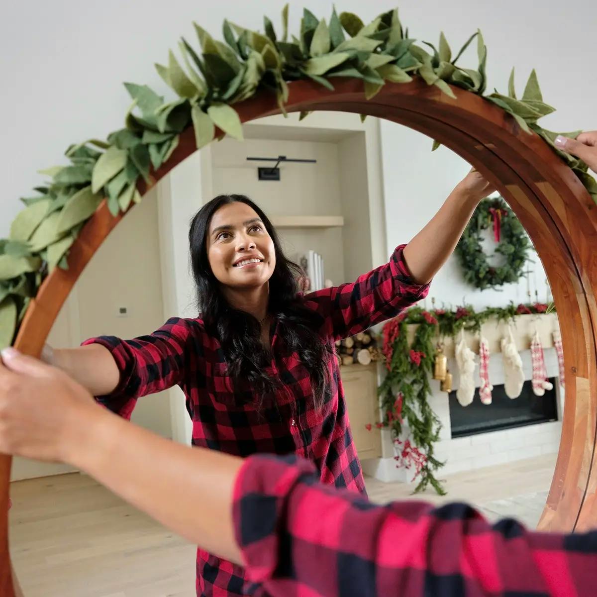 A woman hanging a Christmas garland made from felt over a mirror.